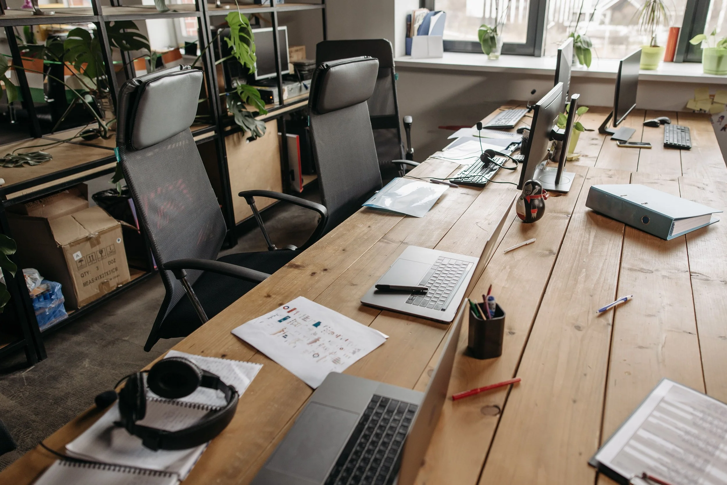 Long wooden desk with office chairs, monitors and a headset in an open workspace